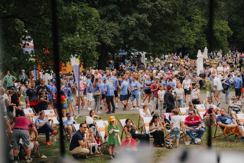 Große Menschenmenge bei einem Outdoor-Event im Park, viele sitzen auf Liegestühlen, umgeben von Bäumen.