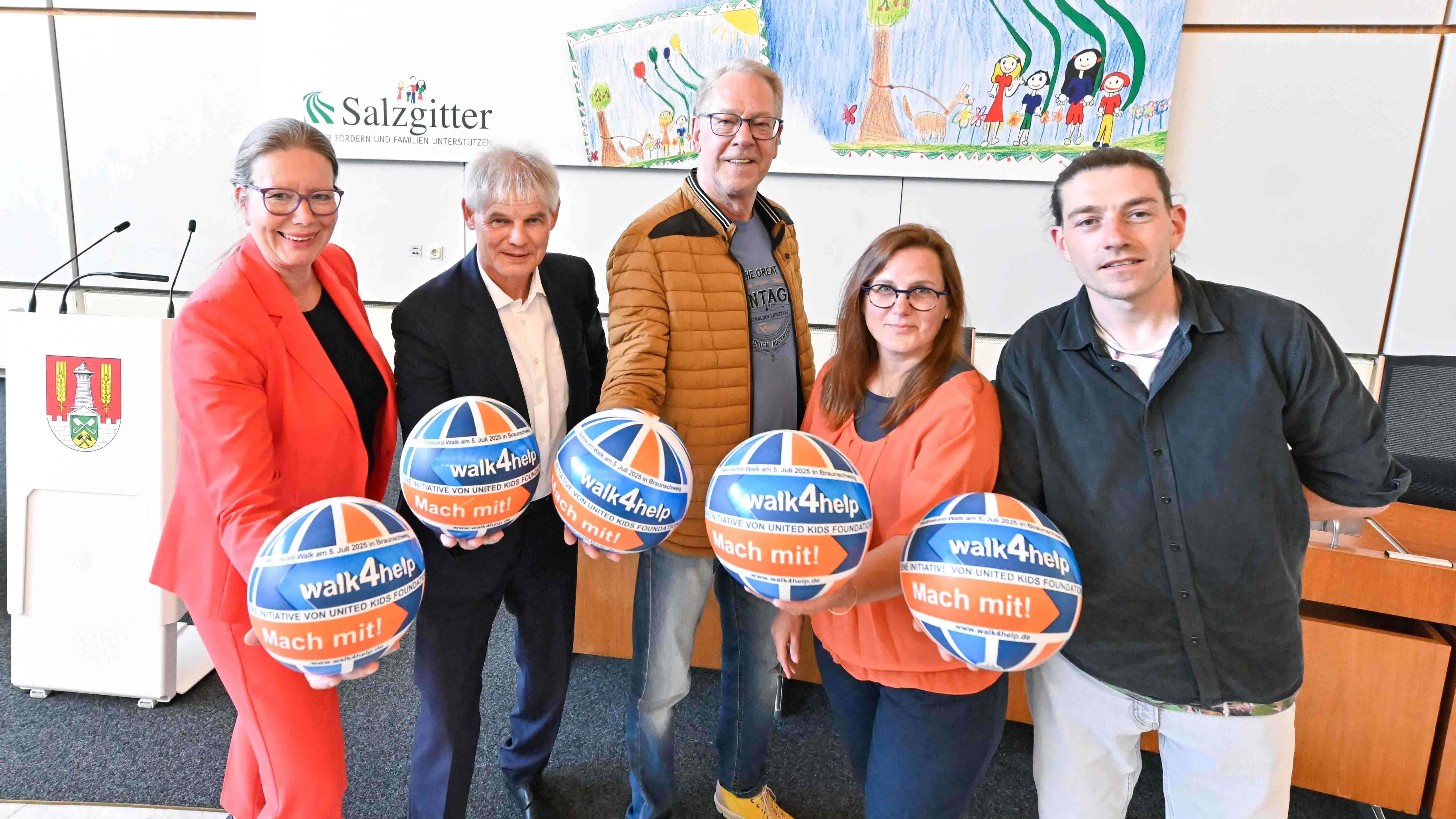 Fünf Personen stehen in einer Reihe und halten einen Ball mit dem Logo des walk4help in einer Hand, diesen strecken sie nach vorne Richtung Kamera.