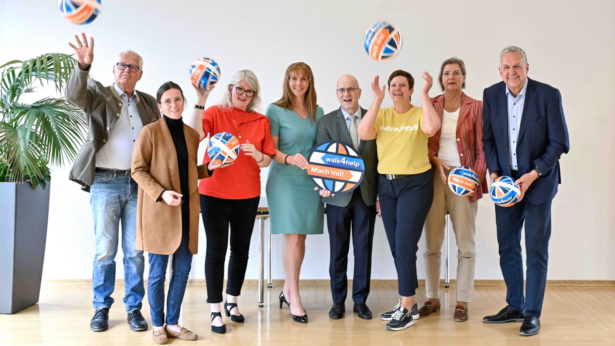 Acht Personen stehen nebeneinander und halten einen Ball in der Hand oder werfen diesen gerade hoch. Zwei Personen halten das Logo des walk4help in der Hand.