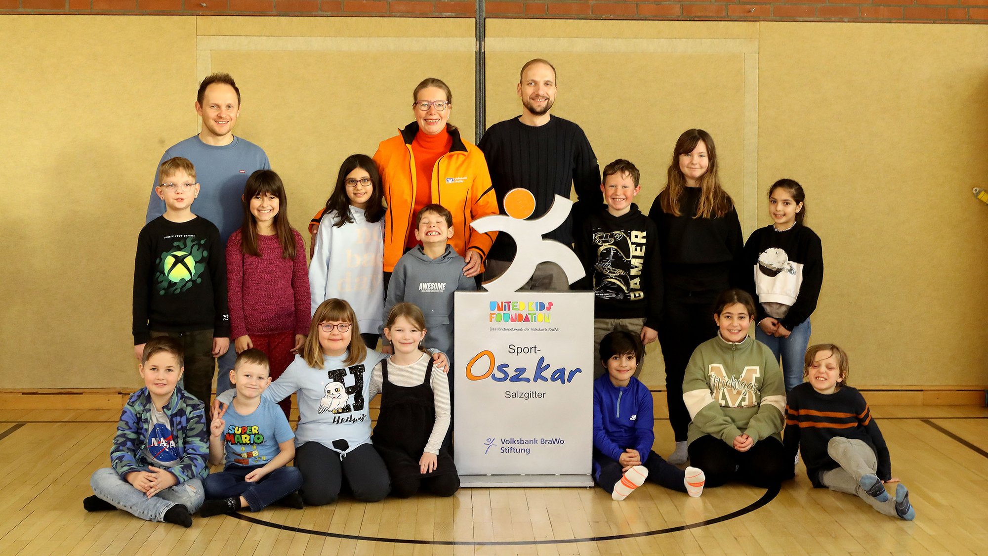 Eine Gruppe Kinder stehen gemeinsam mit drei Erwachsenen in einer Sporthalle. 