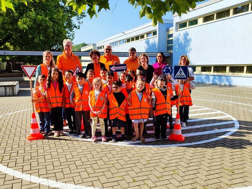 Gruppenbild der Stadtjugendfeuerwehr Salzgitter. Die Kinder haben alle eine organgefarbene Weste an und halten verschiedene, verkleinerte Verkehrszeichen an einem Stab.