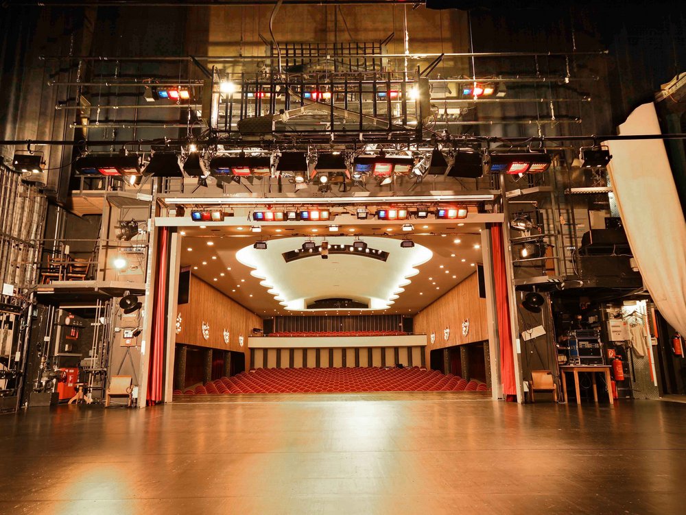 Theaterbühne mit Blick auf den Zuschauerraum mit roten Sitzen.