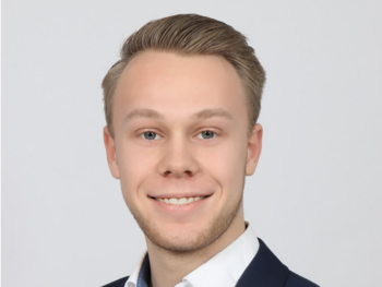 Ein lächelnder Mann in einem weißen Hemd und dunklen Sakko. Er hat kurzes, blondes Haar und blickt freundlich in die Kamera. Der Hintergrund ist einfarbig hell.