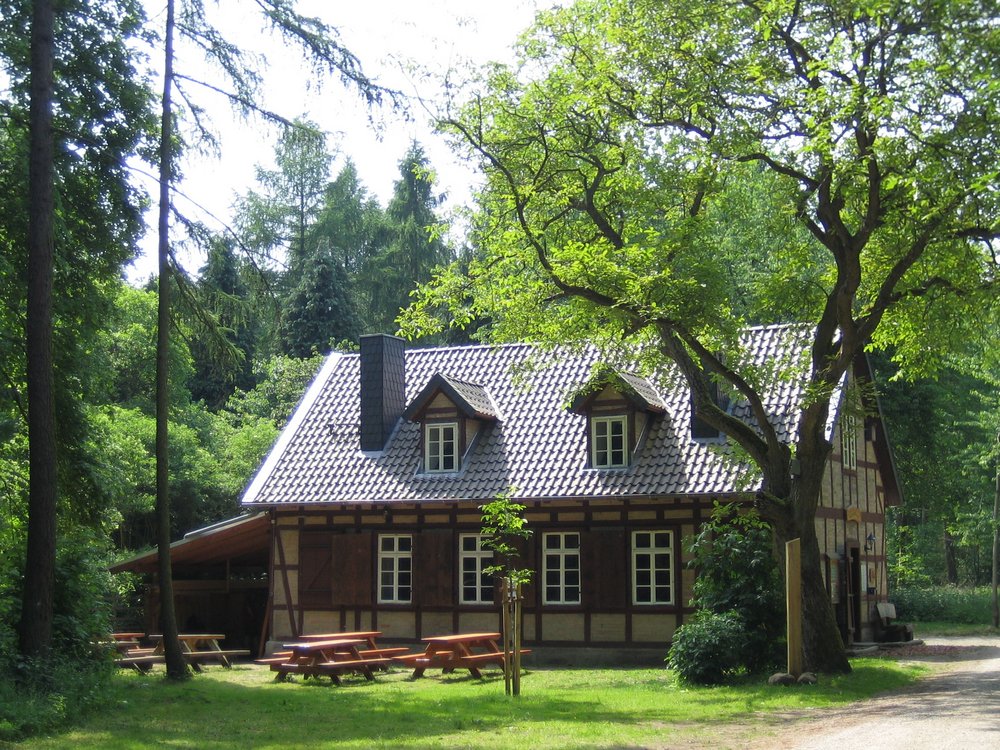 Fachwerkhaus umgeben von Bäumen. Vor dem Haus stehen mehrere Picknick Sitzgruppe.