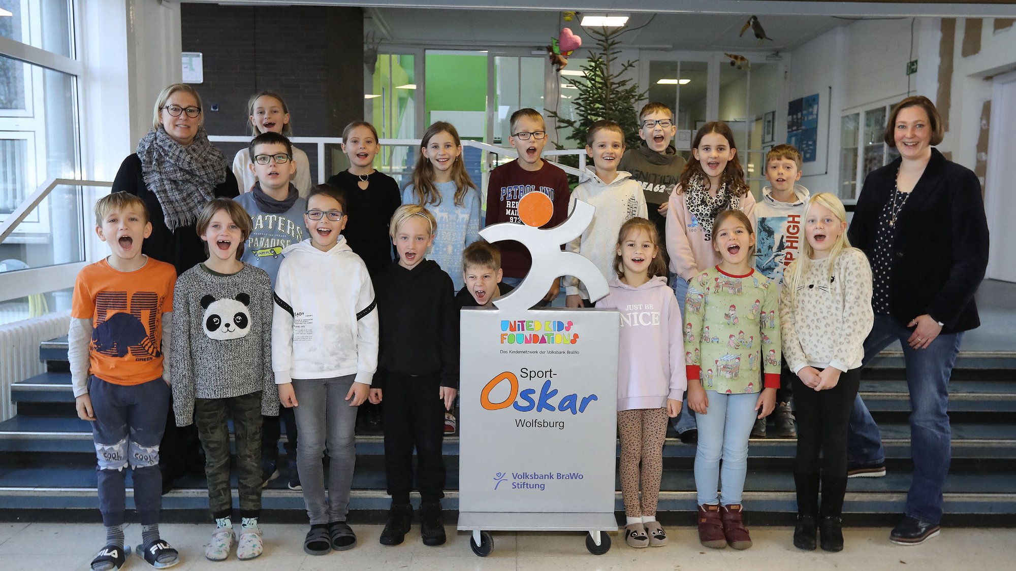 Eine Gruppe von Kindern stehen lachend, mit zwei Erwachsenen auf einer Treppe.