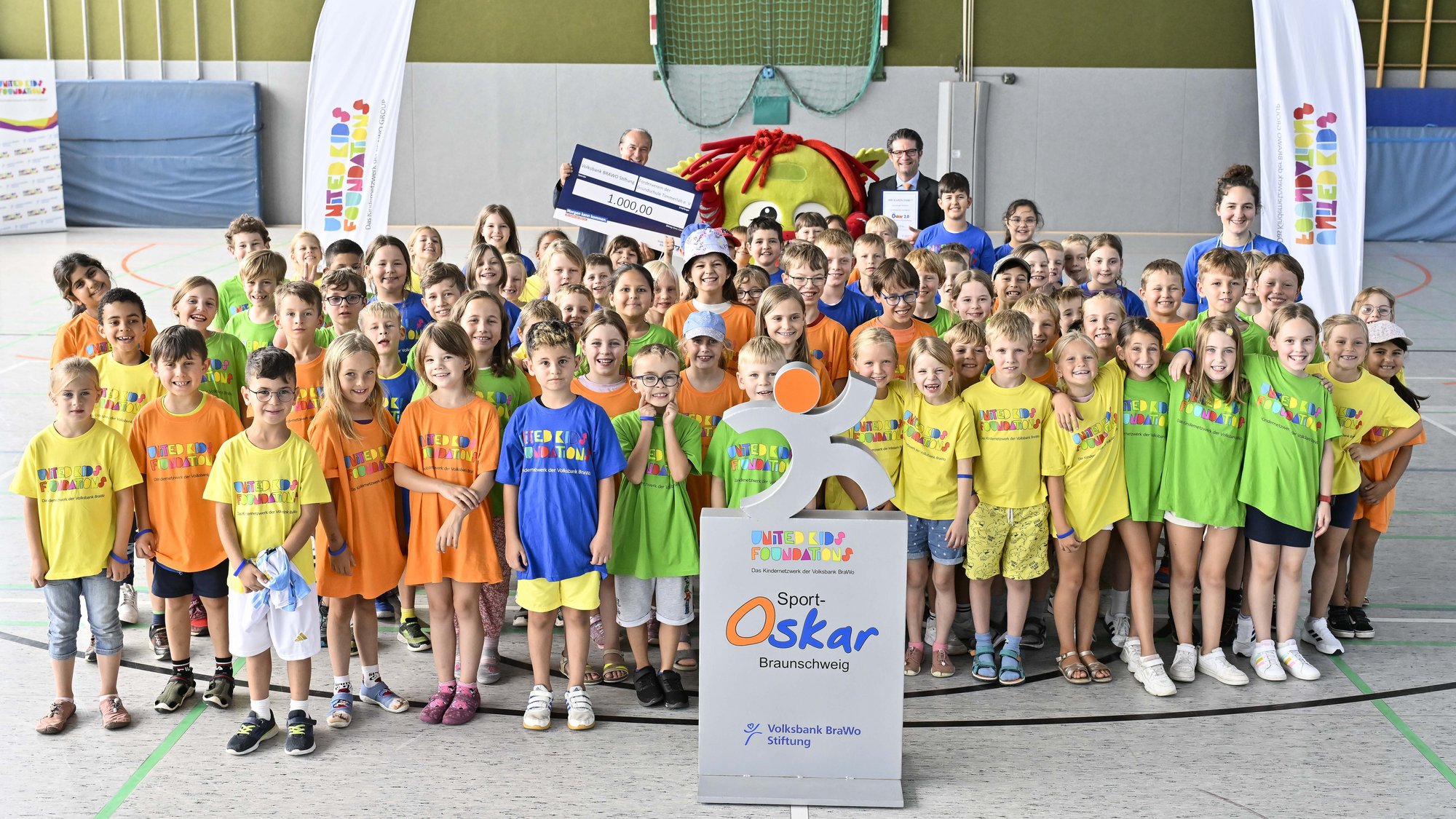 Große Gruppe von Kindern stehen in bunten Tshirts in einer Turnhalle.